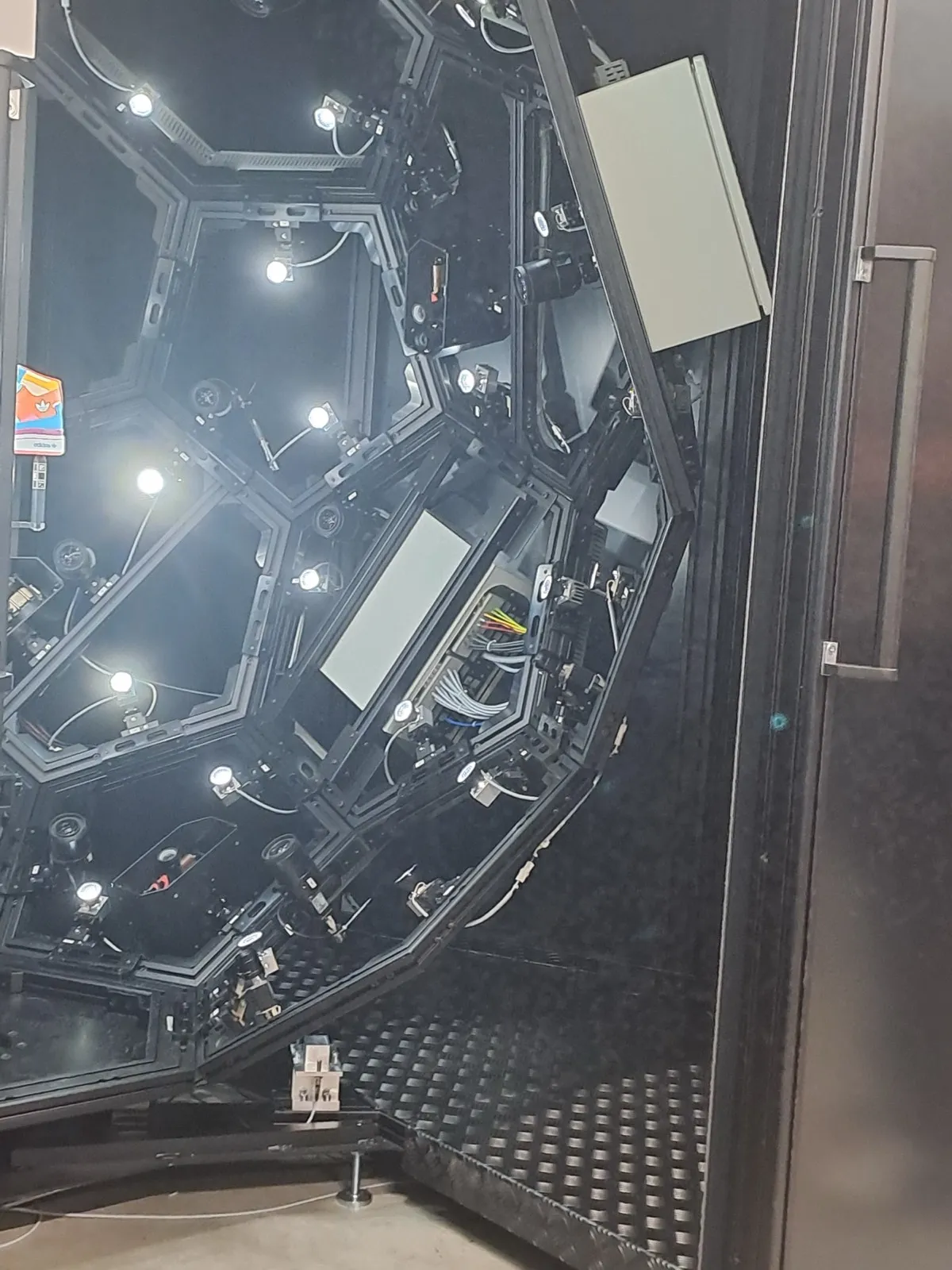 Inside view of an octagonal camera rig with dozens of studio lights and cables mounted around a small central platform inside a black enclosure
