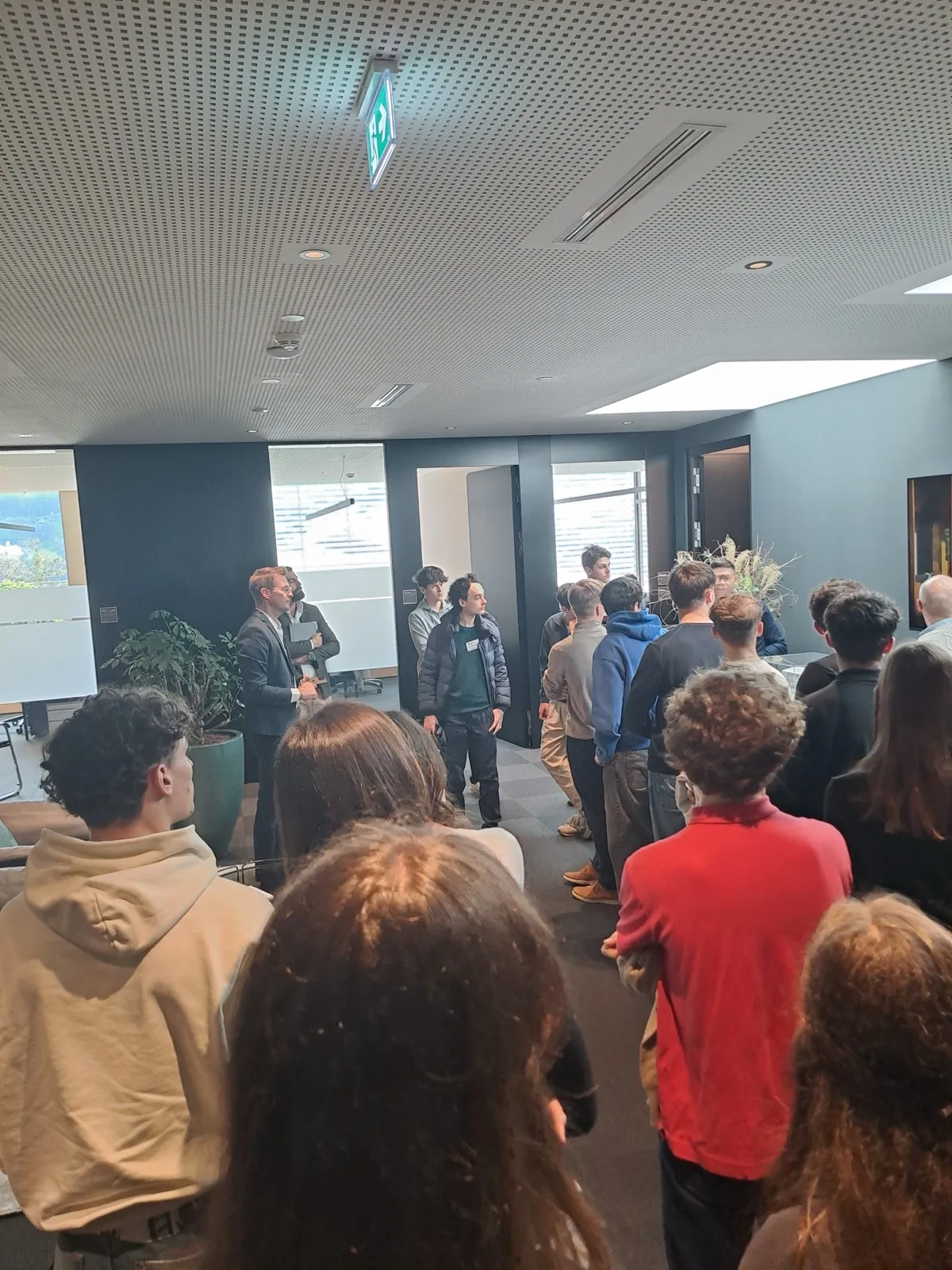 A group of participants entering a modern lobby together, following an organiser toward a glass doorway