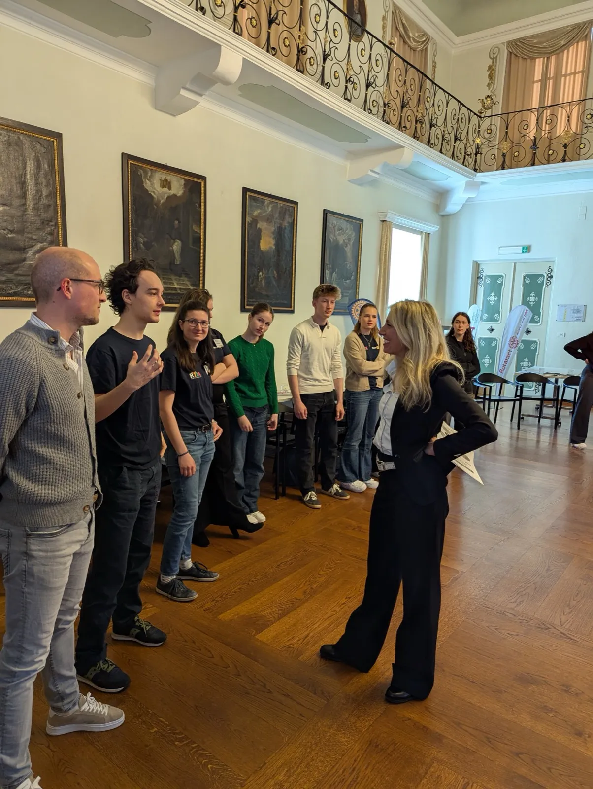 A small group of participants standing and talking together in a hall lined with dark historic paintings