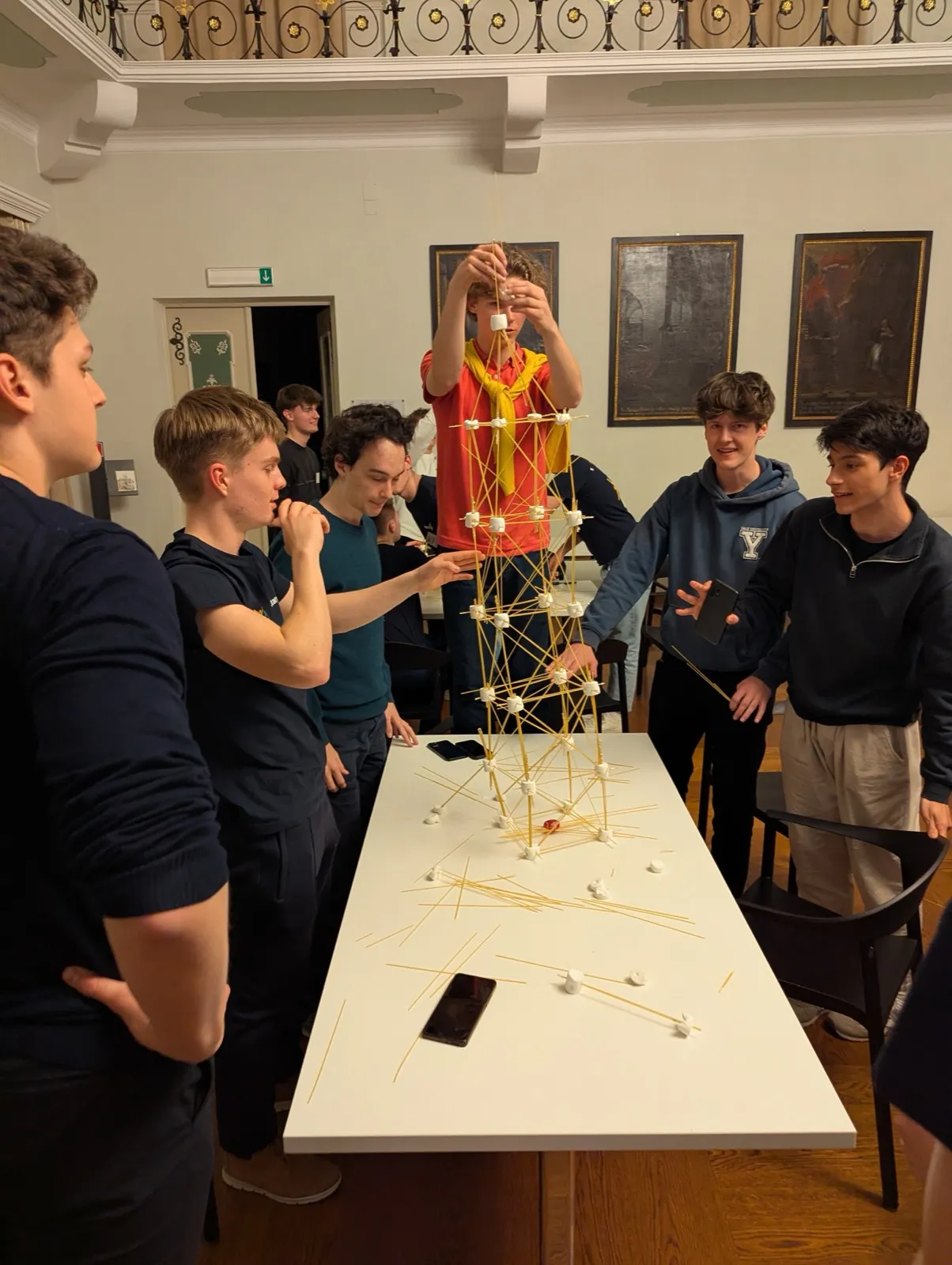 A cheering group of participants raising a completed marshmallow and spaghetti tower above their table