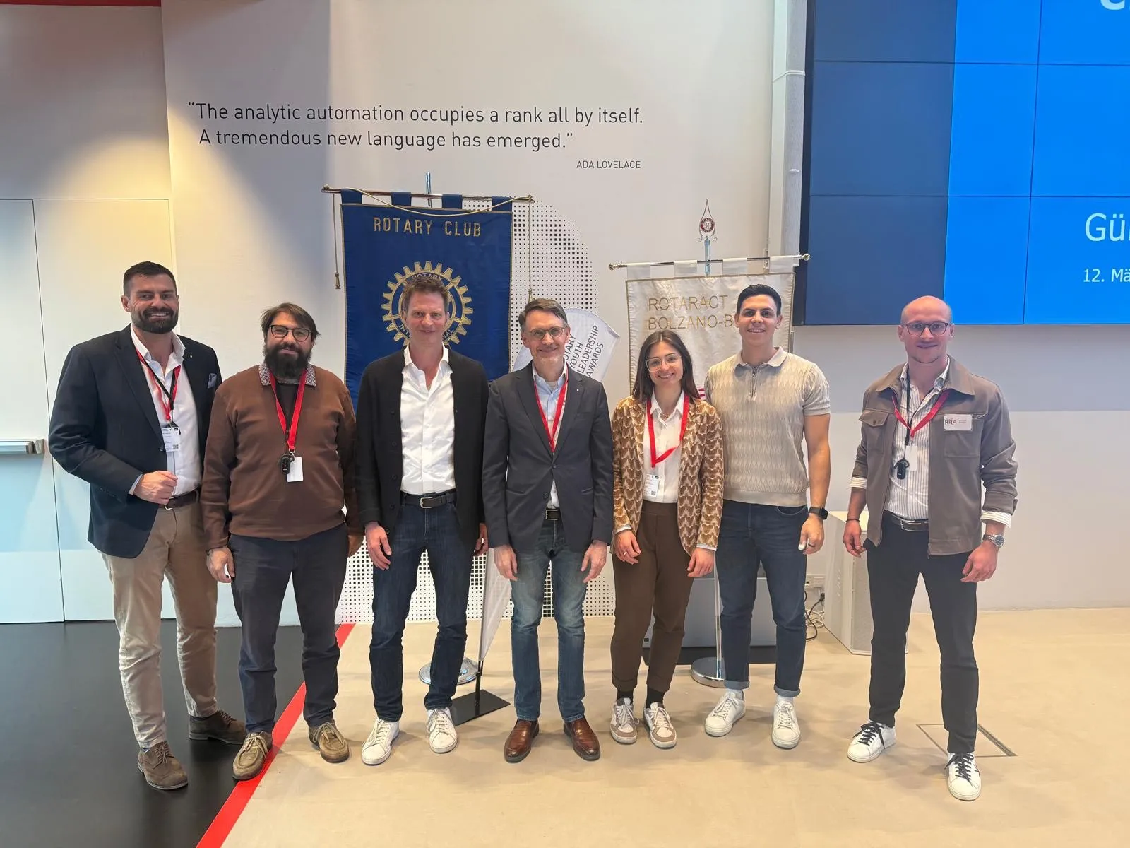 A group of organisers posing together in front of Rotary and partner club banners beneath a printed wall quotation
